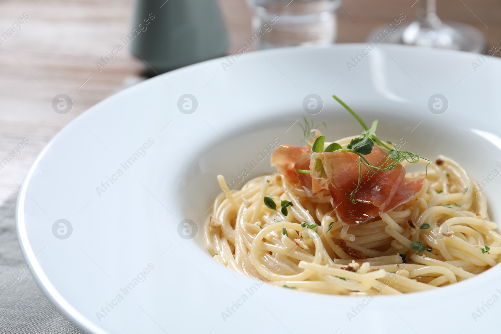 Photo of Tasty spaghetti with prosciutto and microgreens on plate, closeup. Exquisite presentation of pasta dish