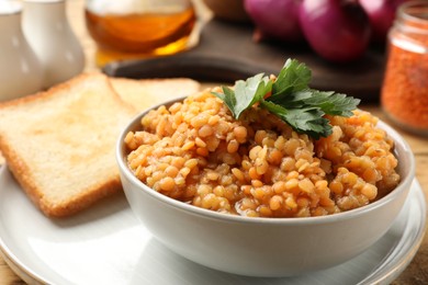 Delicious red lentils with parsley in bowl served on table, closeup