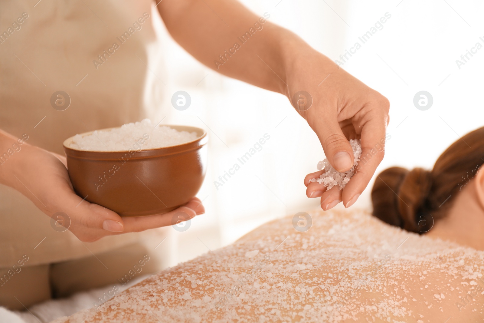 Photo of Young woman having body scrubbing procedure with sea salt in spa salon, closeup