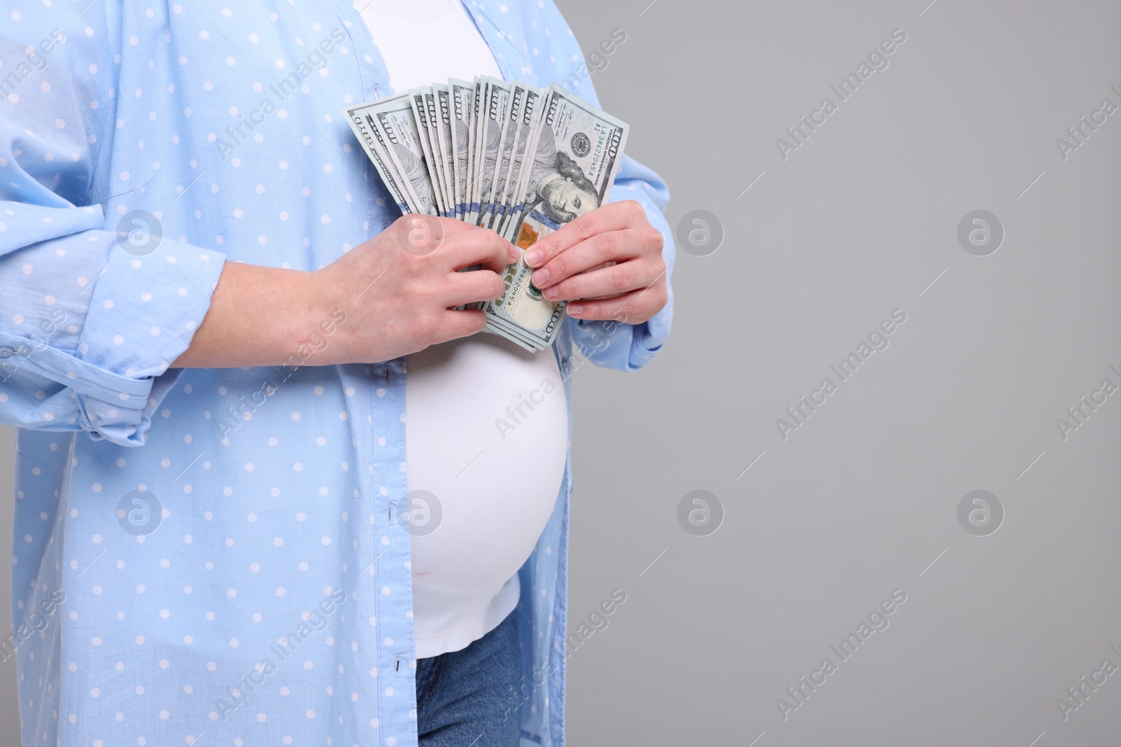 Photo of Surrogate mother. Pregnant woman with dollar banknotes on light grey background, closeup. Space for text