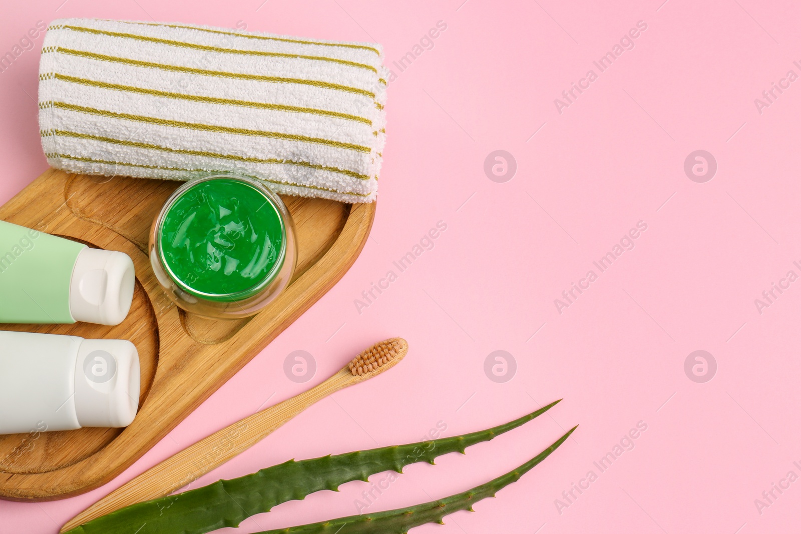 Photo of Tubes of toothpaste, fresh aloe, toothbrush and towel on pink background, flat lay. Space for text