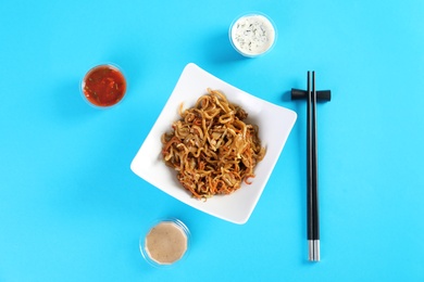 Chinese noodles served with chopsticks and different sauces on color background, top view. Food delivery