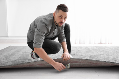 Worried man hiding money under carpet indoors. Financial savings