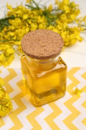 Photo of Rapeseed oil in glass bottle and beautiful yellow flowers on table, closeup