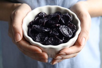 Woman holding bowl of dried plums, closeup. Healthy fruit