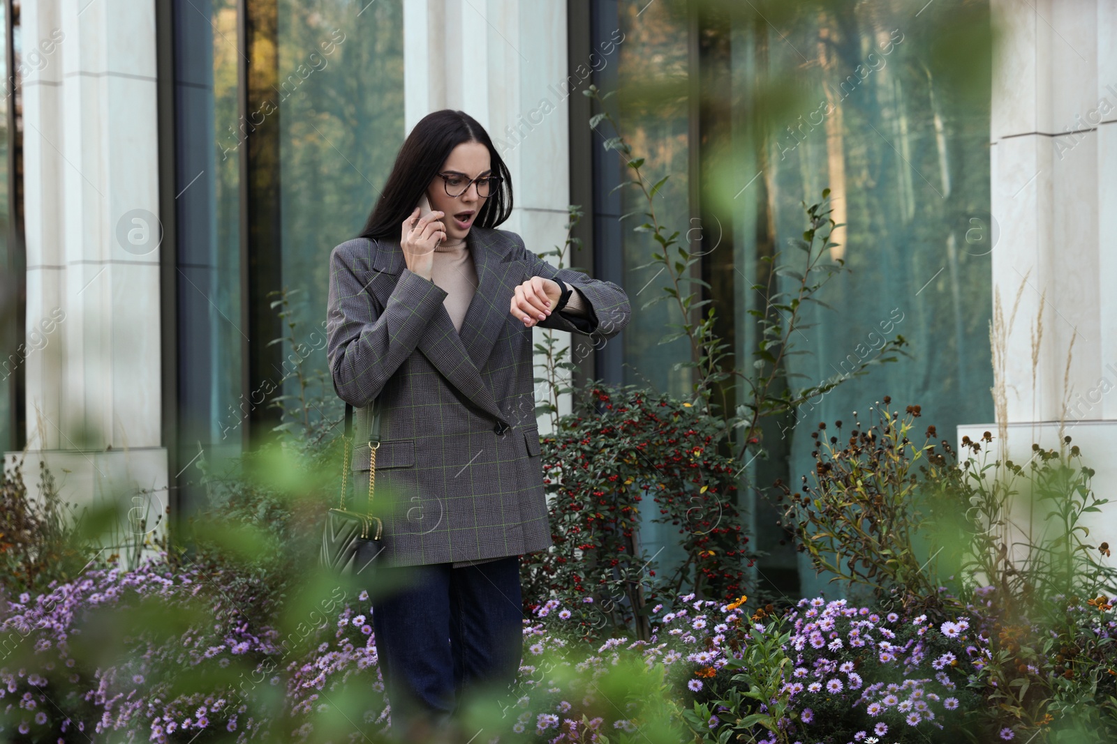 Photo of Emotional woman checking time while talking on smartphone outdoors. Being late concept