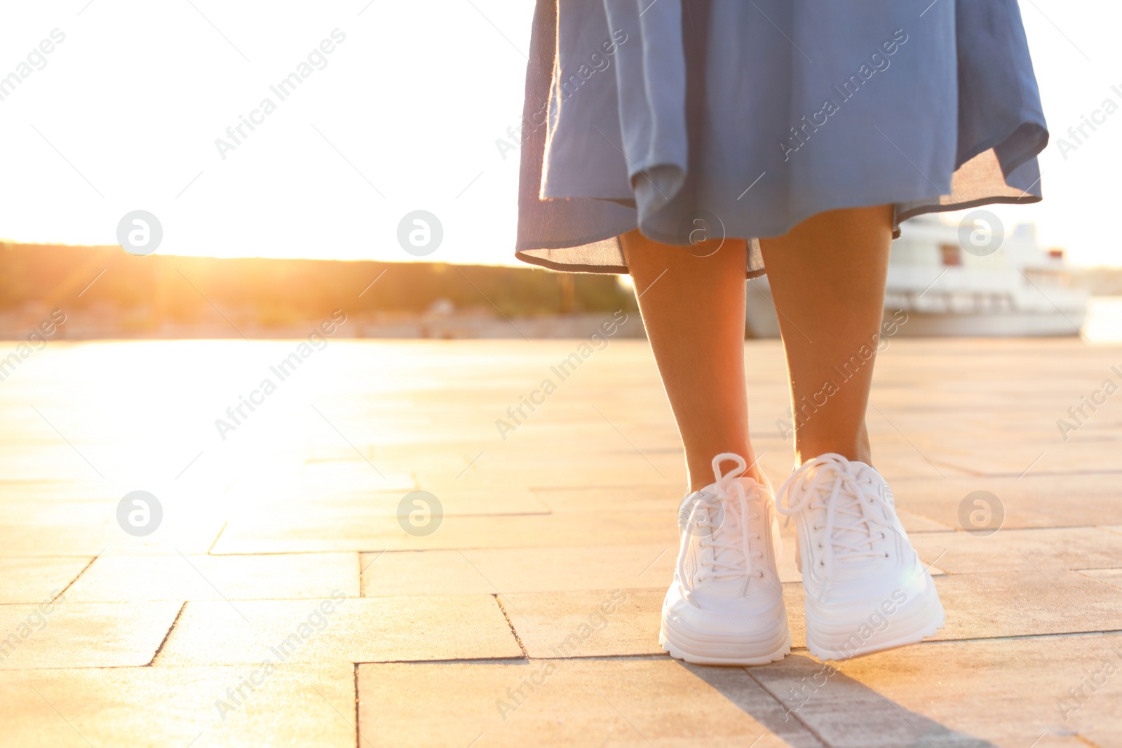 Photo of Young woman walking on pier at sunset light. Space for text