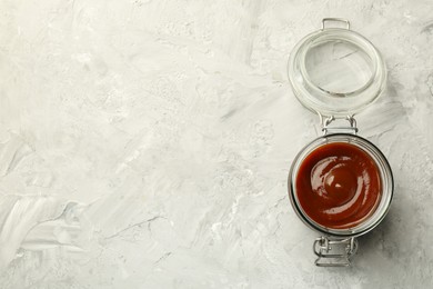 Photo of Tasty barbeque sauce in open jar on grey textured table, top view. Space for text