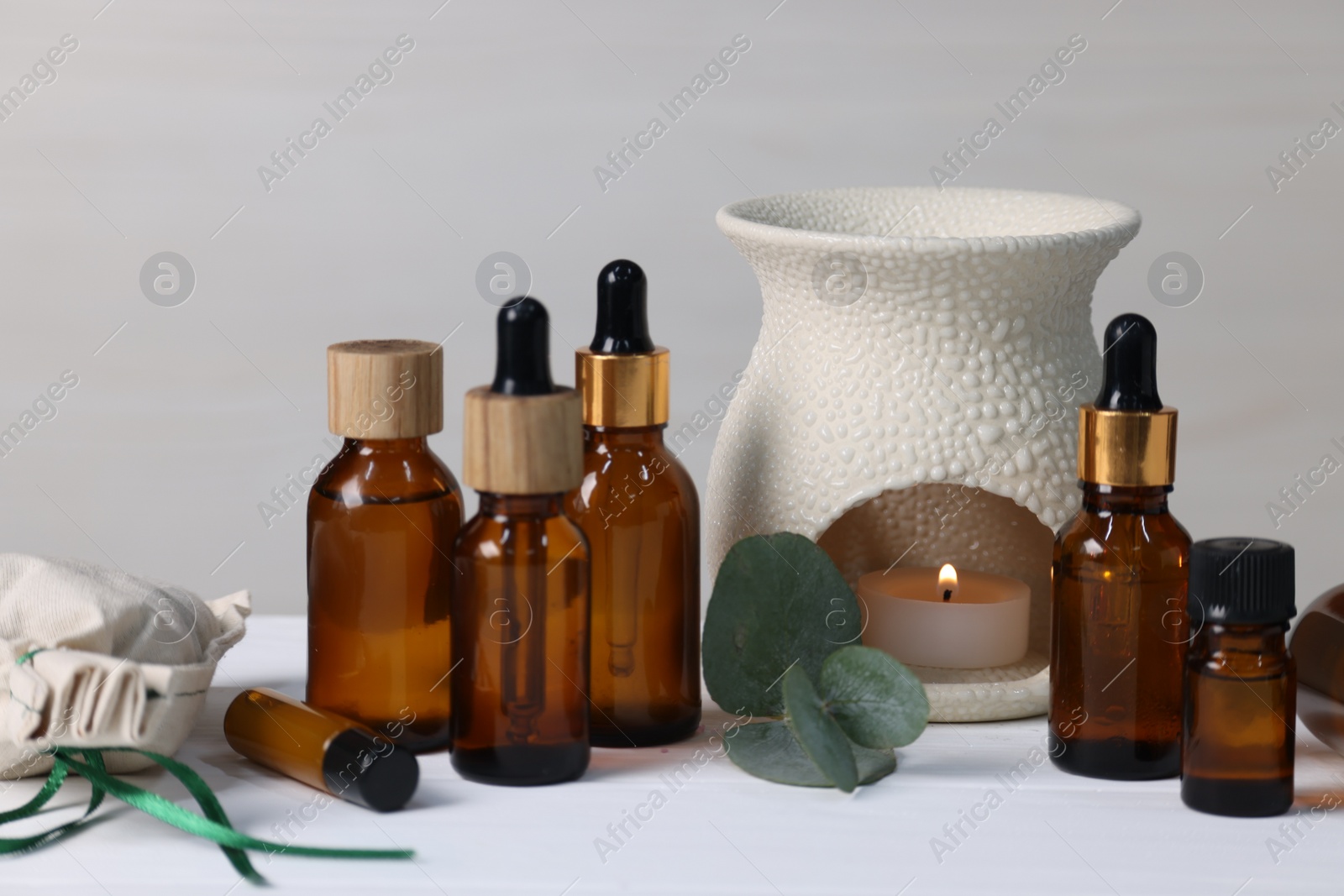 Photo of Different aromatherapy products, burning candle and eucalyptus leaves on white wooden table against light background