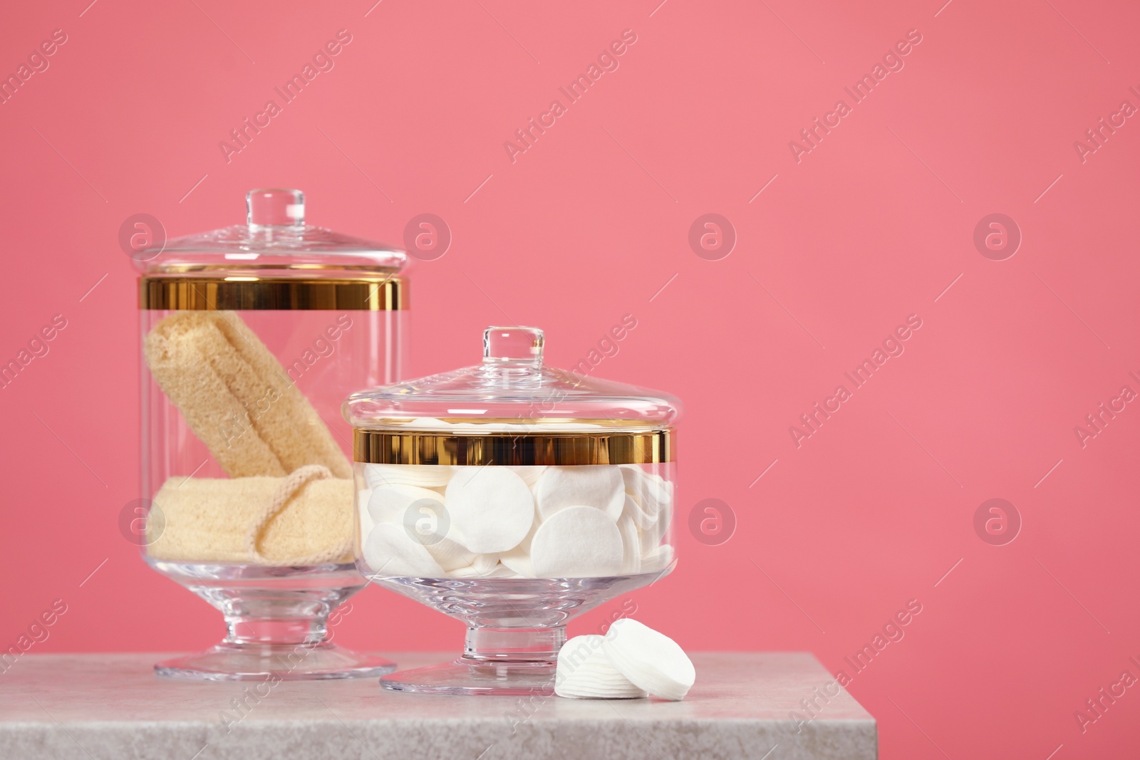 Photo of Composition of glass jars with cotton pads on table against pink background. Space for text