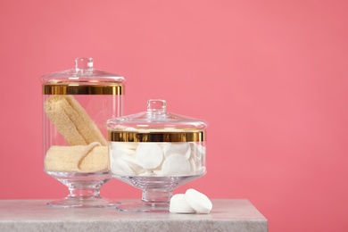 Composition of glass jars with cotton pads on table against pink background. Space for text