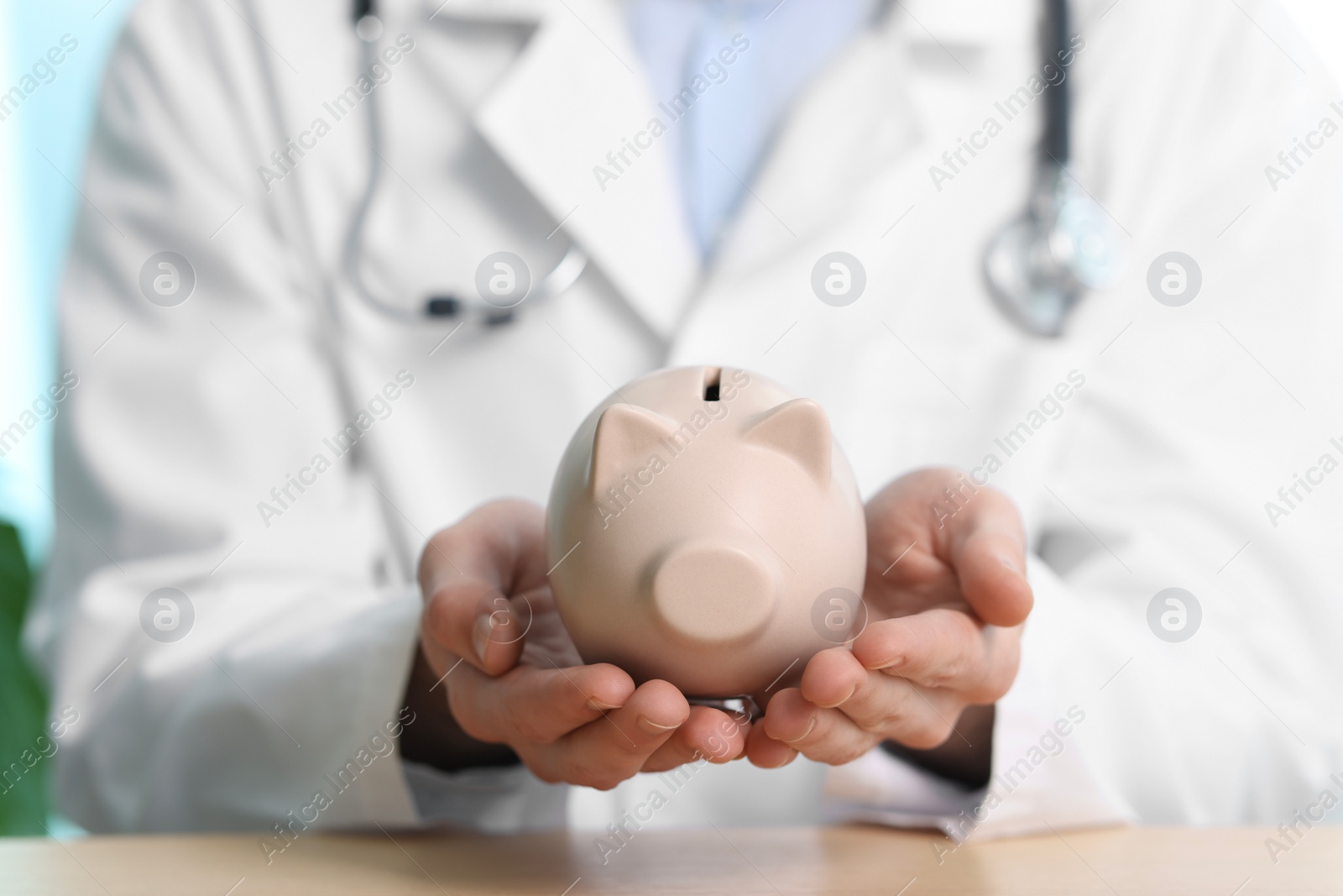 Photo of Doctor with piggy bank at table, closeup