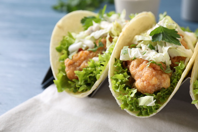 Photo of Yummy fish tacos in holder on blue table, closeup