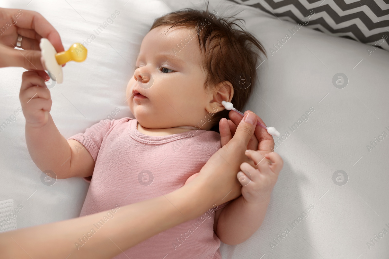 Photo of Mother cleaning ears of her baby with cotton bud on bed, closeup