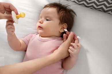 Photo of Mother cleaning ears of her baby with cotton bud on bed, closeup