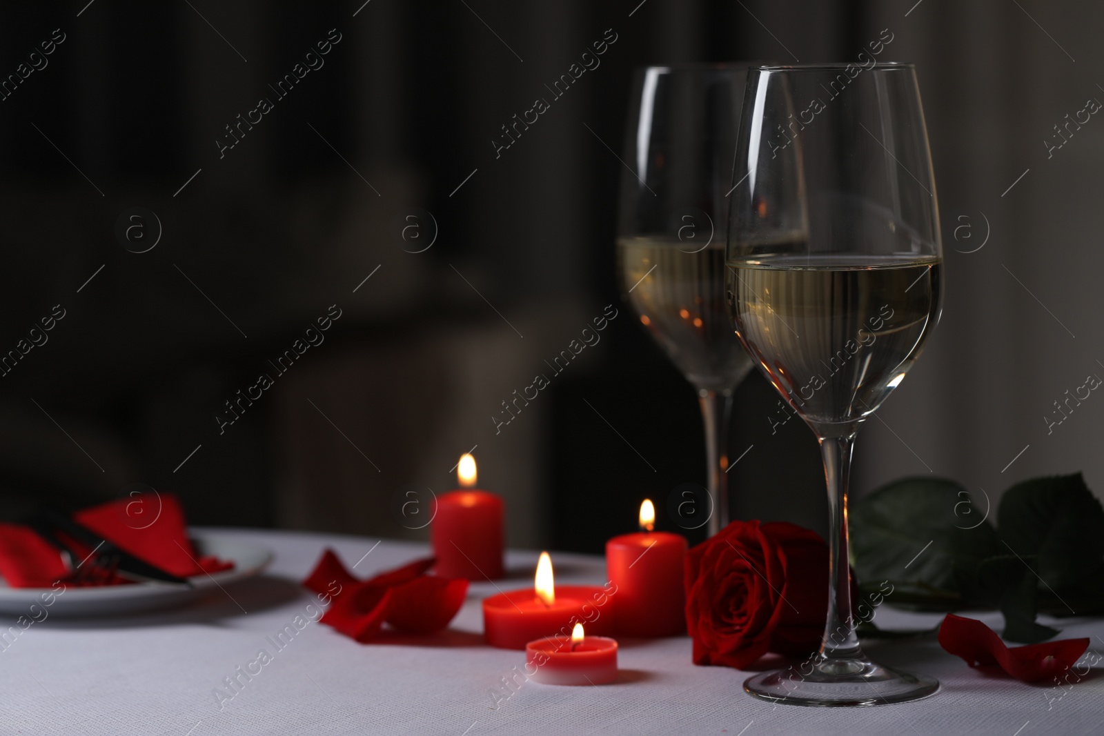 Photo of Romantic table setting with glasses of white wine and burning candles against blurred background, space for text