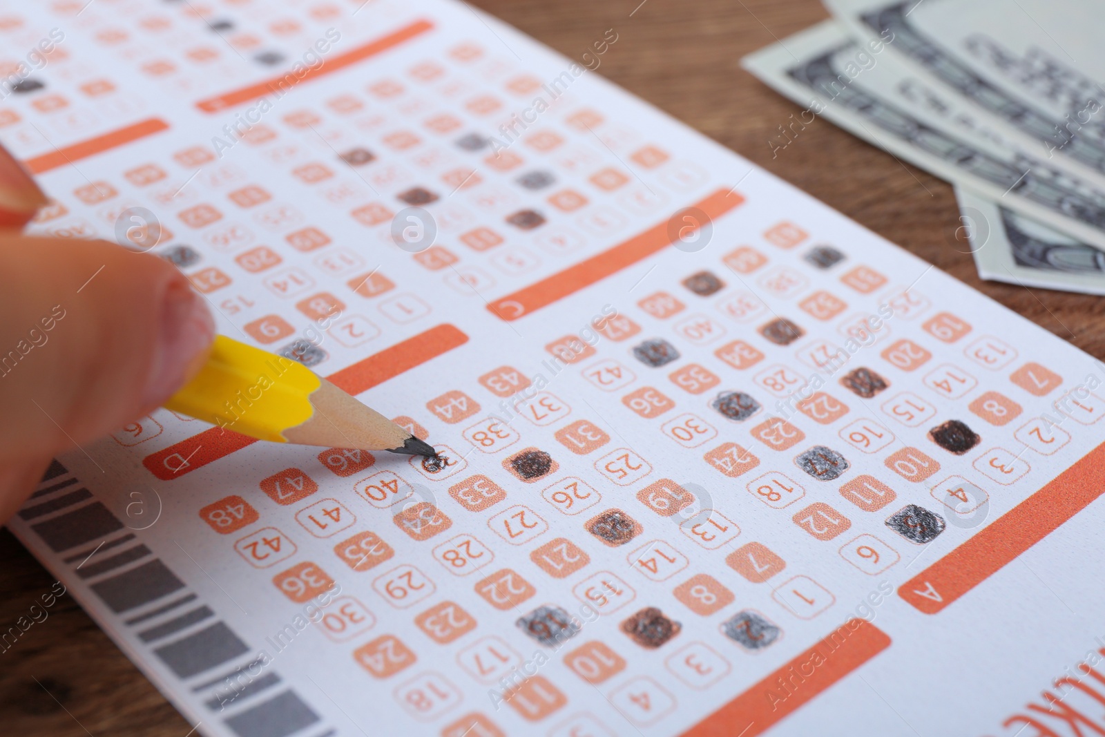 Photo of Woman filling out lottery ticket with pencil on wooden table, closeup. Space for text