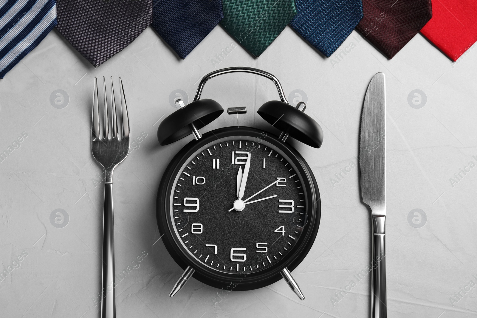 Photo of Business lunch concept. Alarm clock, cutlery and ties on light gray table, flat lay