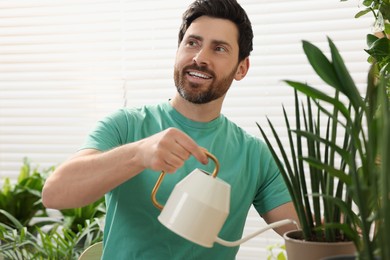 Photo of Man watering beautiful potted houseplants at home