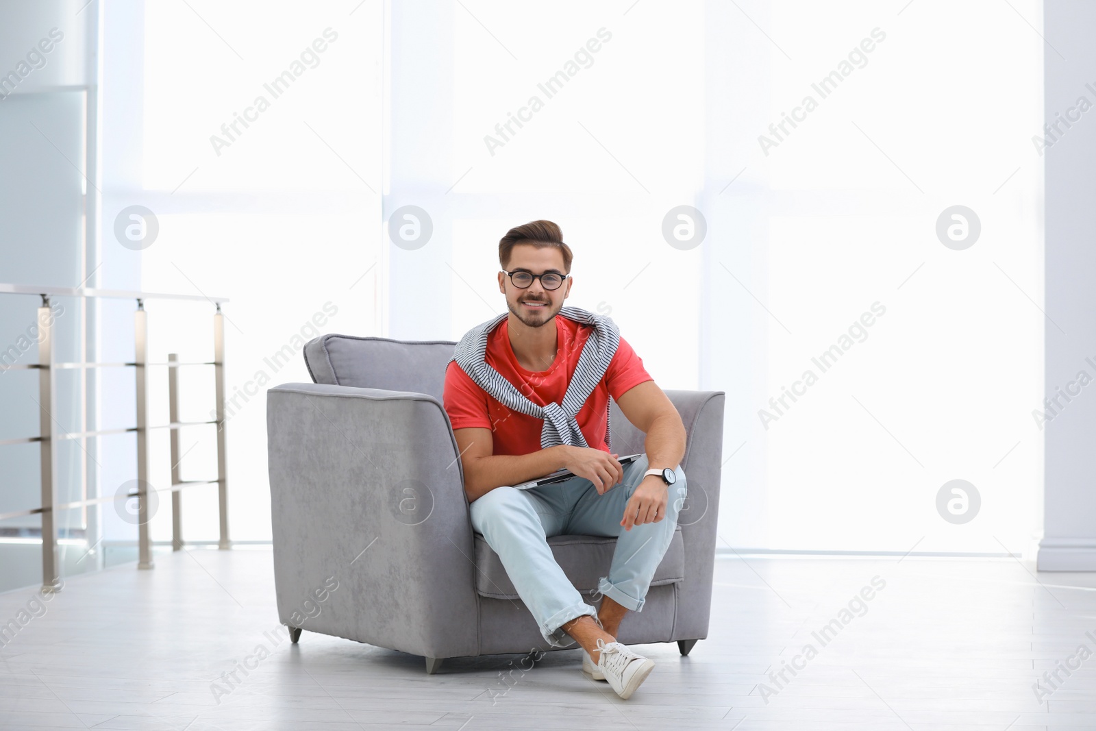Photo of Handsome young man with laptop in armchair indoors. Space for text