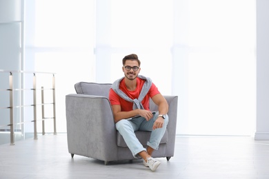 Handsome young man with laptop in armchair indoors. Space for text