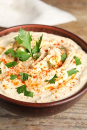 Photo of Tasty hummus with parsley and paprika in brown bowl on wooden table, closeup