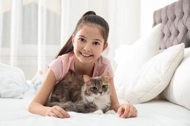 Cute little girl with cat lying on bed at home. First pet