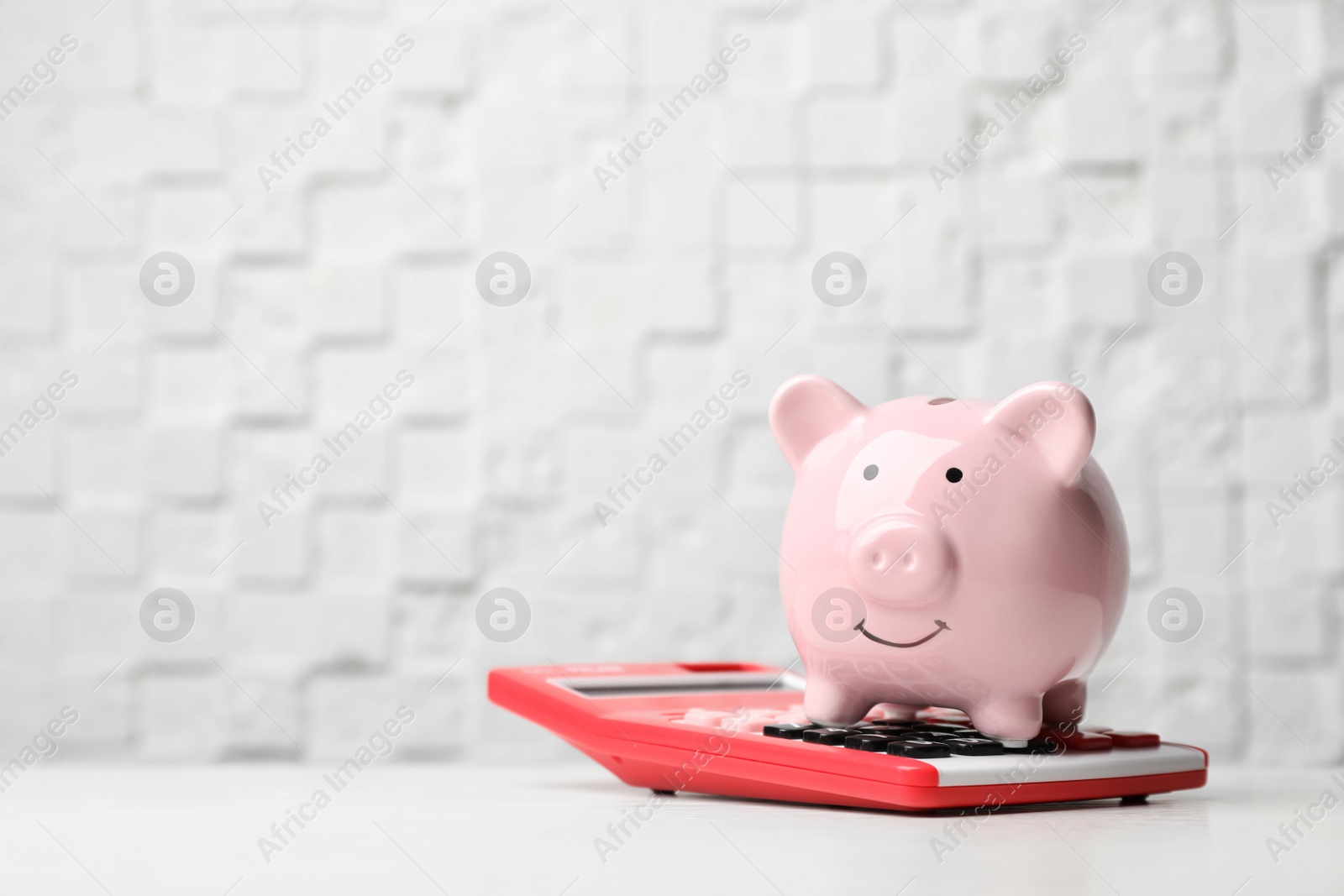 Photo of Piggy bank with calculator on light table. Space for text