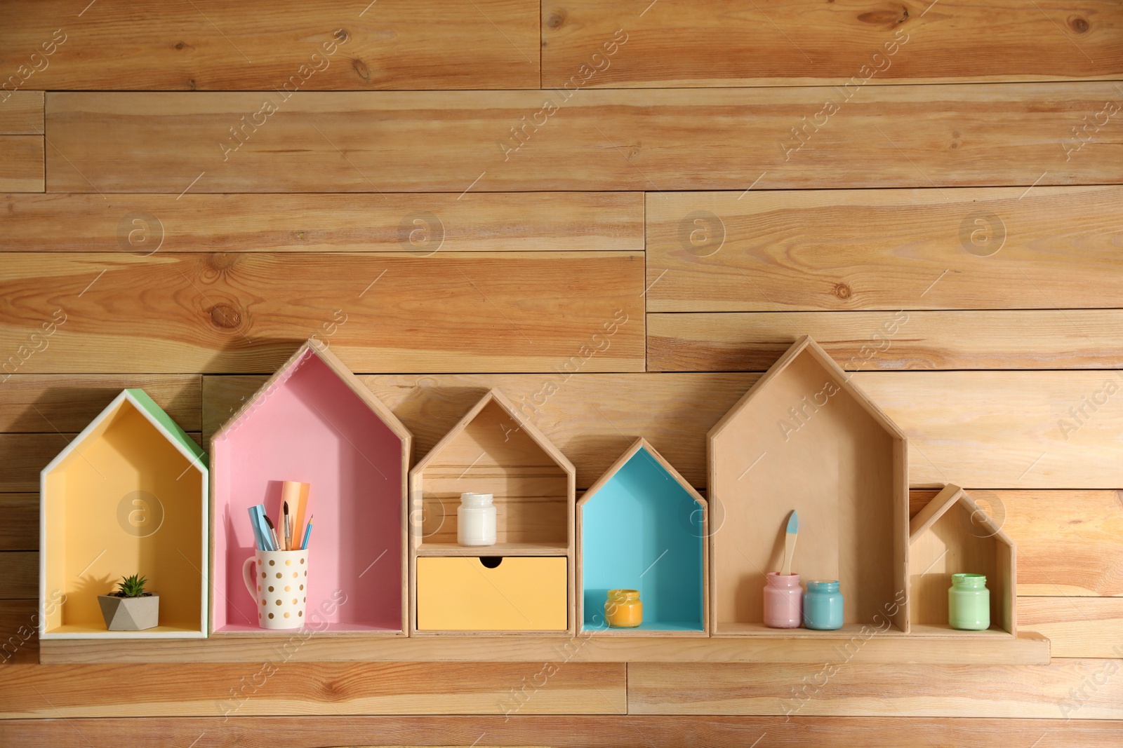 Photo of Painted house shaped shelves with different items on wooden wall. Interior elements