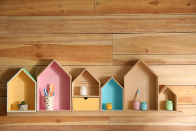 Painted house shaped shelves with different items on wooden wall. Interior elements