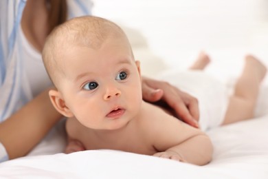 Photo of Woman applying body cream onto baby`s skin on bed, closeup