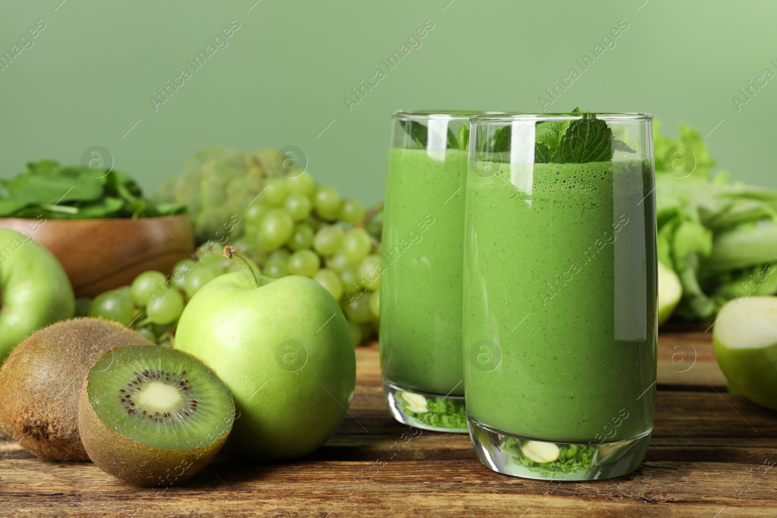 Photo of Green smoothie in glasses and fresh ingredients on wooden table