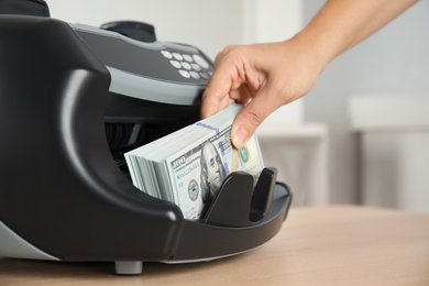 Woman taking money from counting machine at table indoors, closeup