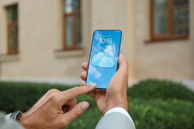 Man checking weather using app on smartphone outdoors, closeup. Data and illustration of cloud on screen