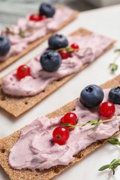 Photo of Tasty cracker sandwiches with cream cheese, blueberries, red currants and thyme on white board, closeup