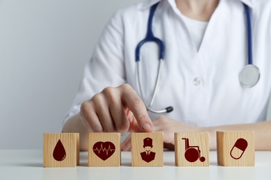 Image of Doctor and wooden cubes with different icons on white table, closeup. Insurance concept