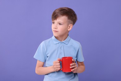 Photo of Cute boy with red ceramic mug on violet background