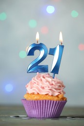 Photo of 21th birthday. Delicious cupcake with number shaped candles for coming of age party on light blue table