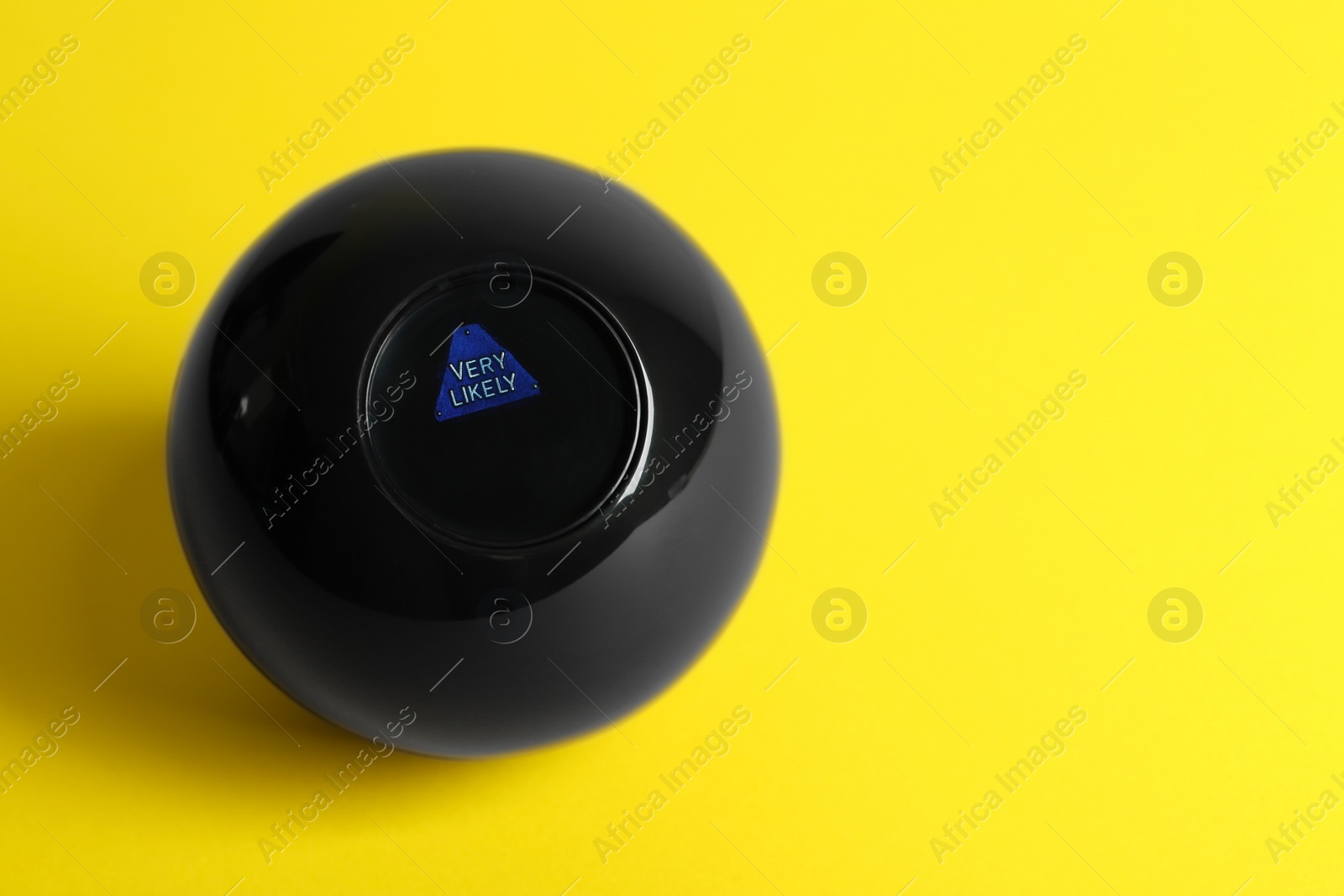 Photo of Magic eight ball with prediction Very Likely on yellow background, above view. Space for text