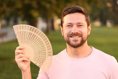Happy man holding hand fan in park