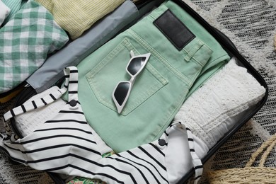 Photo of Open suitcase with summer clothes and sunglasses on floor, above view