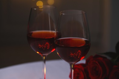 Photo of Glasses of red wine, rose flowers and burning candle against blurred lights. Romantic atmosphere