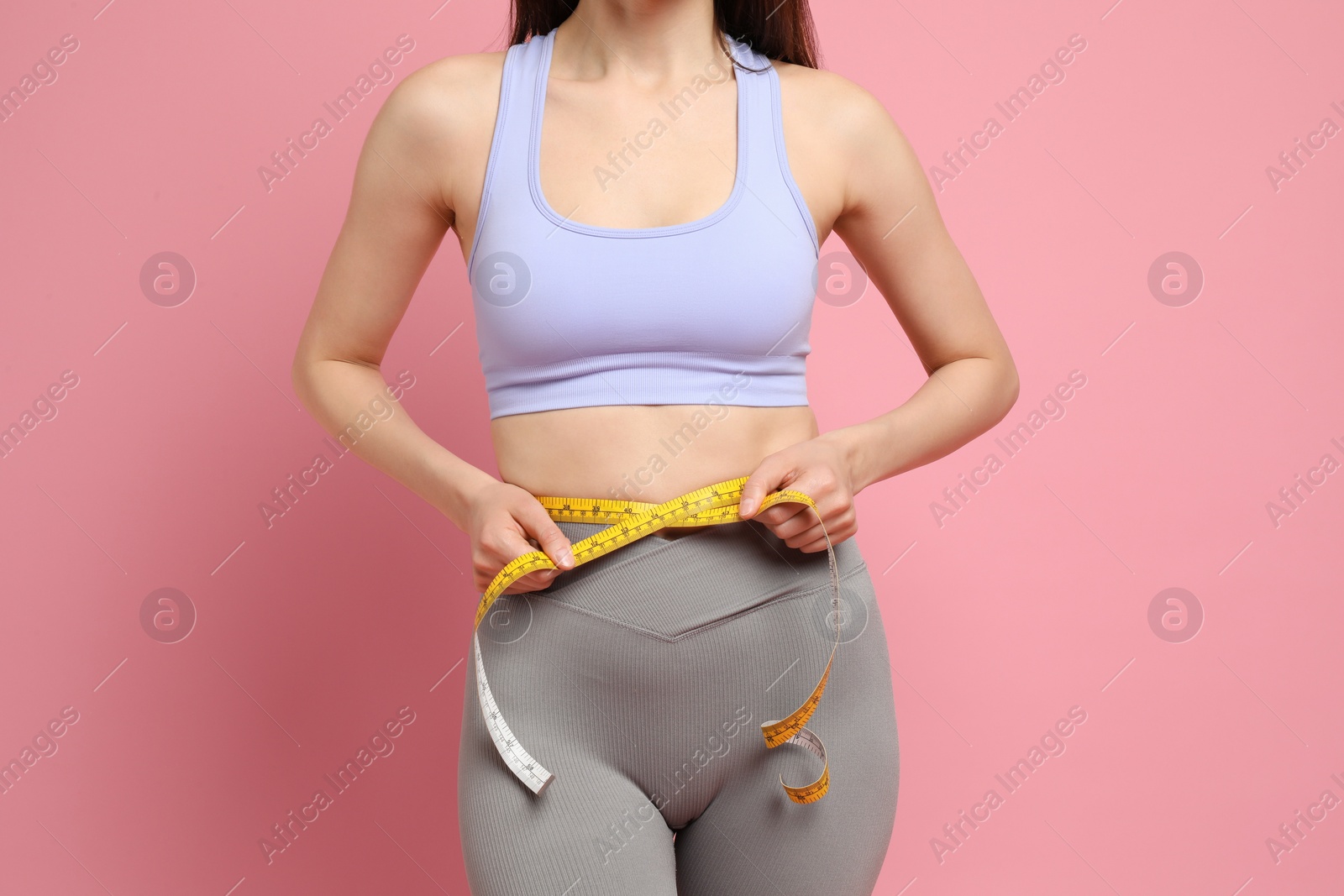 Photo of Woman with measuring tape showing her slim body on pink background, closeup