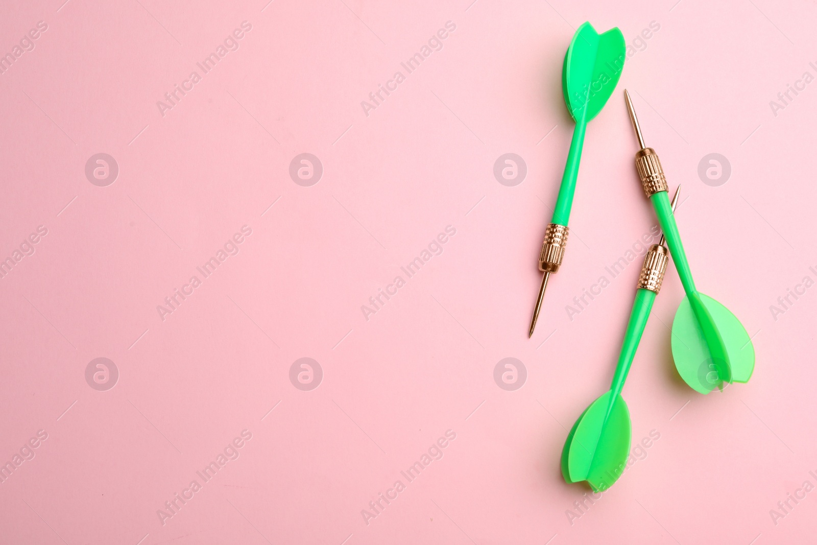 Photo of Green dart arrows on pink background, flat lay with space for text