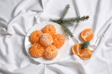 Photo of Peeled delicious ripe tangerines and fir branches on white bedsheet, flat lay