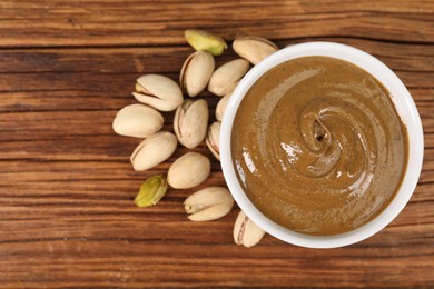 Photo of Delicious nut butter in bowl and pistachios on wooden table, top view