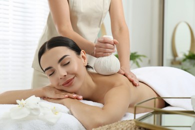 Photo of Young woman receiving herbal bag massage in spa salon