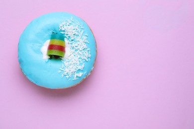 Photo of Tasty glazed donut decorated with coconut shavings and rainbow sour candy on purple background, top view. Space for text