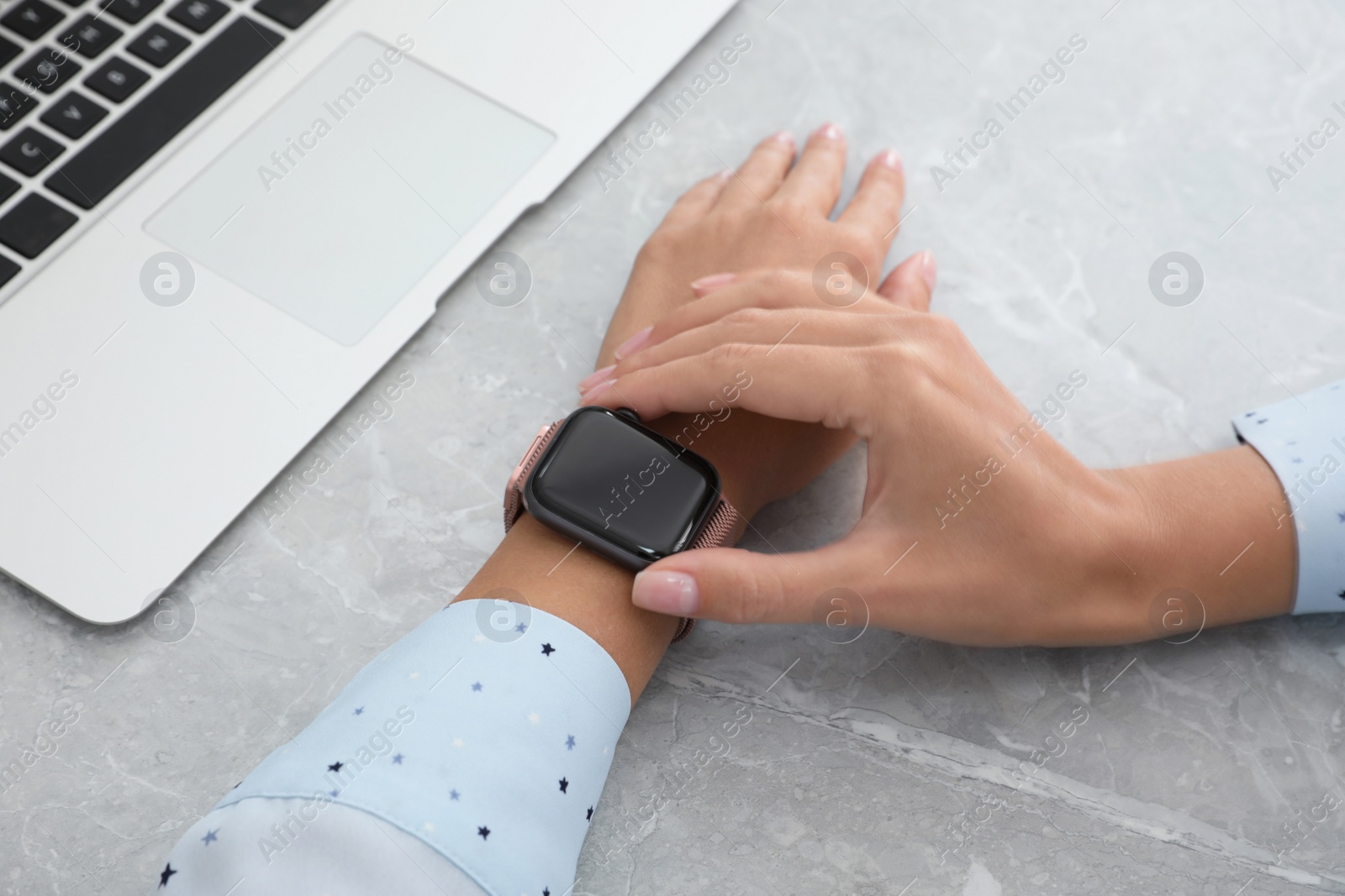 Image of Woman checking stylish smart watch at grey marble table, closeup