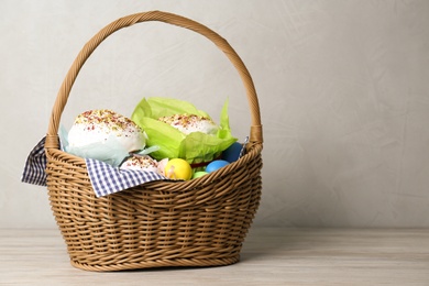 Photo of Basket with delicious Easter cakes and dyed eggs on light wooden table. Space for text